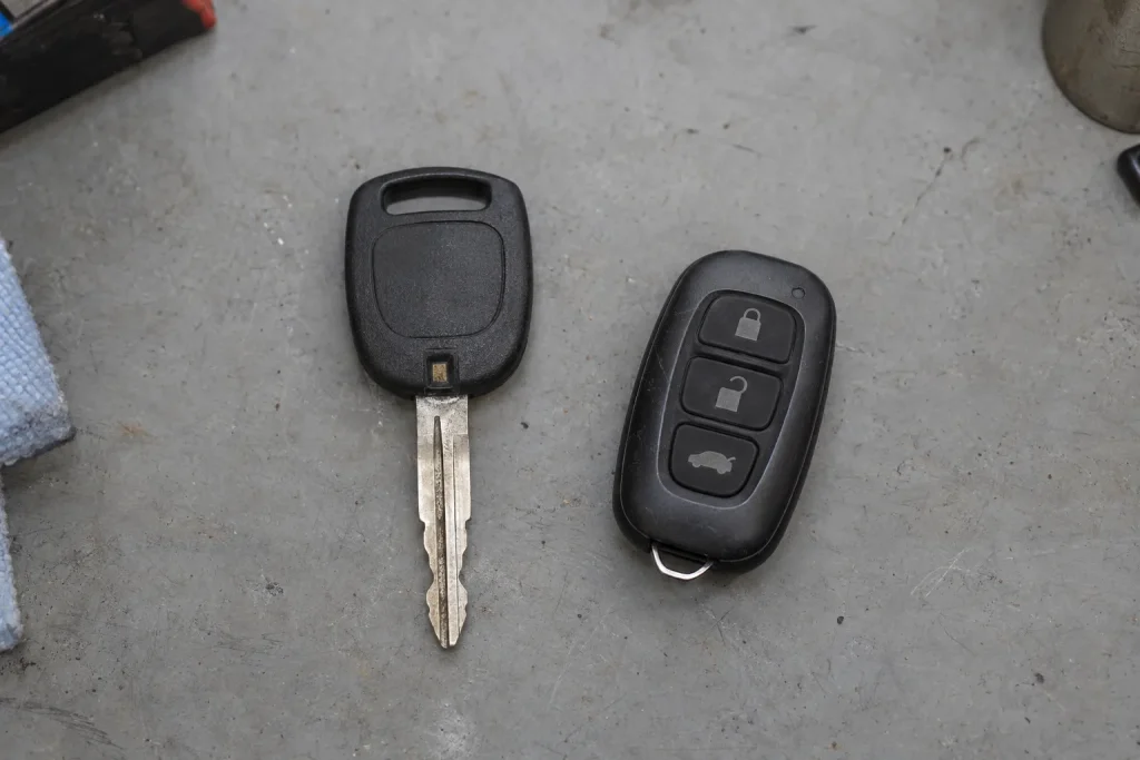 A transponder key and a key fob placed side by side on a neutral grey desk surface under even workshop lighting.