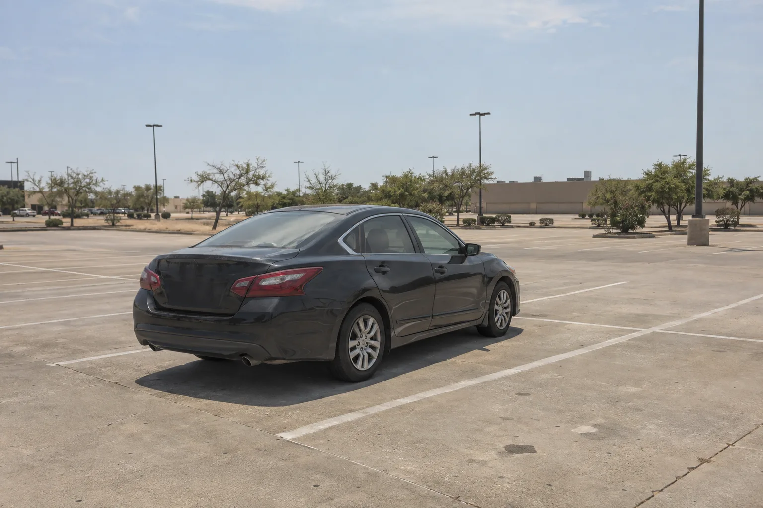 A dark sedan sits alone on sun-scorched asphalt in a Texas parking lot under blazing midday sun, with heat shimmer rising from the pavement and a flat commercial roofline visible in the background.