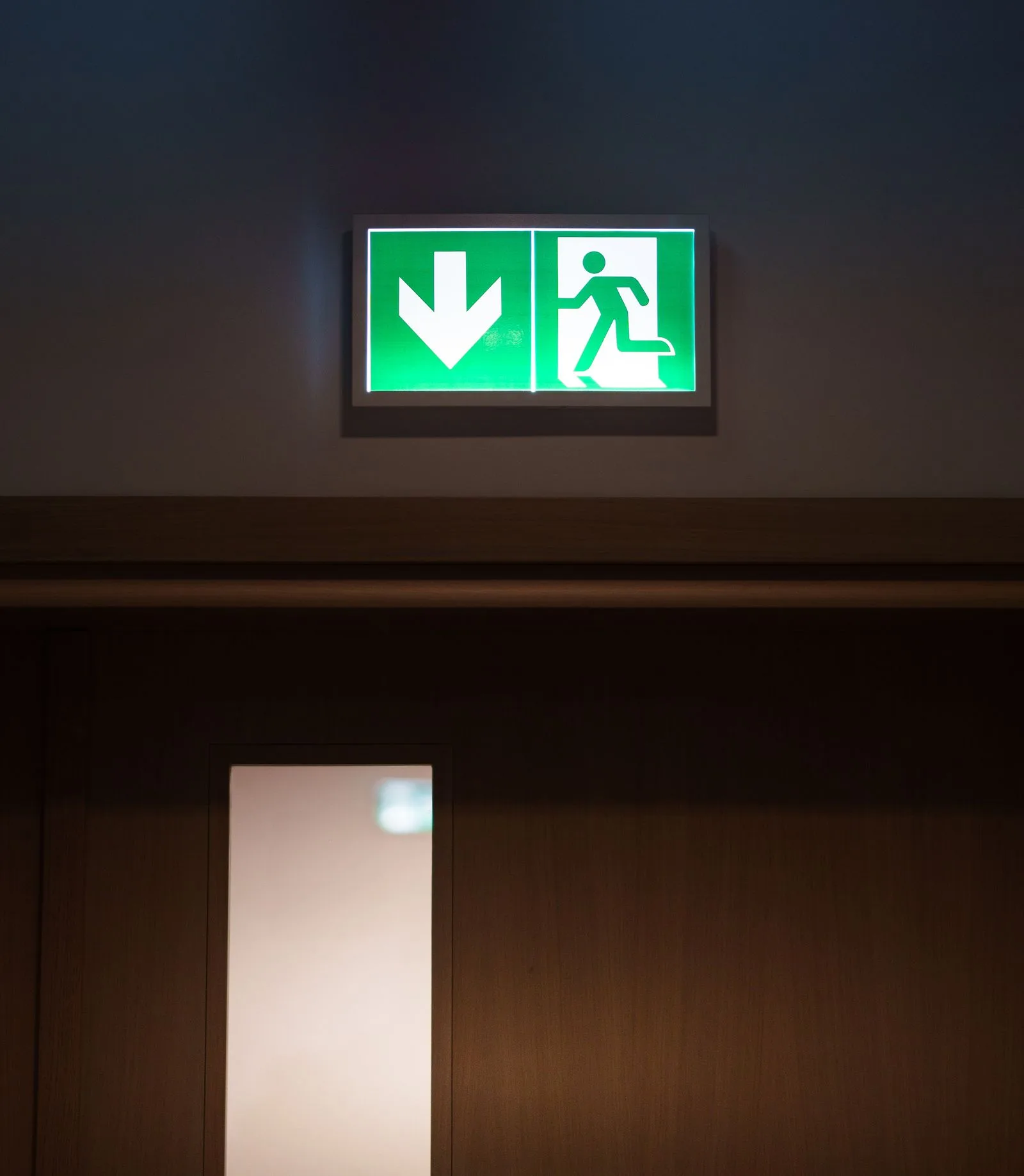 Illuminated green emergency exit sign above a closed exit door