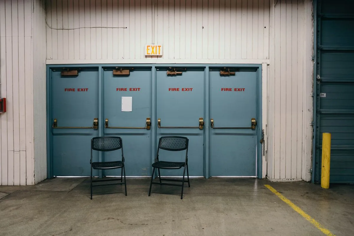 Row of blue fire exit doors with exit hardware in a commercial warehouse
