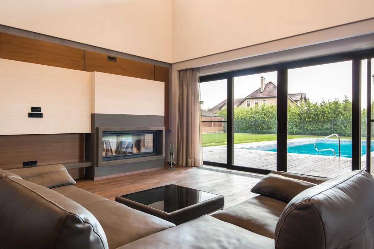 Glass sliding doors opening from a living room to a poolside patio